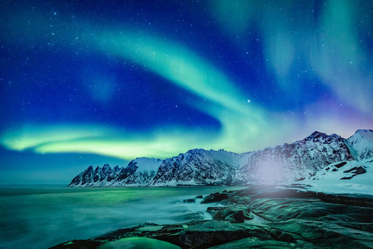 Vivid Northern lights during polar night on Lofoten Islands in Norway. Epic scene of dancing aurora borealis in the night sky over jagged mountain ridge and Arctic ocean on island Senja, polar circle.