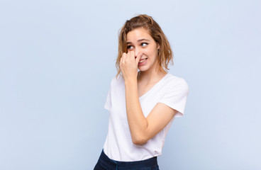 young blonde woman feeling disgusted, holding nose to avoid smelling a foul and unpleasant stench...