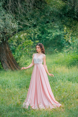 Obraz na płótnie Canvas Cute attractive brunette woman enjoying nature in delicate elegant pink silk dress with white lace top. Image for party graduation prom ball stylish evening outfit celebration. Fashion glamor summer