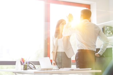 Happy business people giving high-five at desk in office