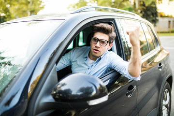 Angry young man clenching his fist, sitting in new car and shouting