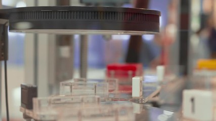 Flashing laser scanner with moving details on automated control system conveyor, people walking on background. Flash of scanning computer-aided quality system. Automatic test set items scan on belt