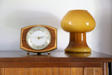 Mid century decor.  Vintage or retro clock in shape focus on a sideboard with a background retro blown glass mushroom lamp