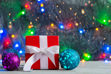 Red gift box with Christmas decorations on bokeh background and garland lights.