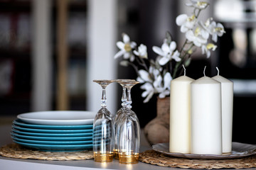 blue plates and wine glasses with a gold rim stand on a table on a stand next to large white candles and a vase of flowers