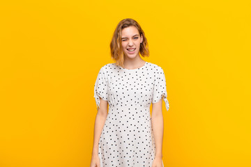 young blonde woman looking happy and friendly, smiling and winking an eye at you with a positive...
