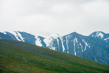 Atmospheric alpine landscape with green mountainside and big mountain ridge with glacier. Green...