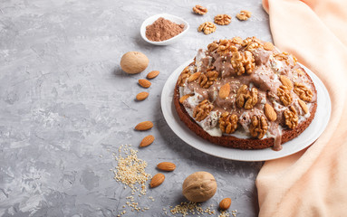 Homemade cake with milk cream, cocoa, almond, hazelnut on a gray concrete  background with orange textile, side view.