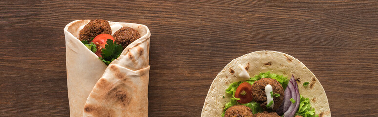 top view of falafel with vegetables and sauce wrapped and unwrapped in pita on wooden table, panoramic shot