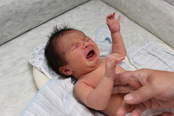 Crying newborn baby on changing table. Cute little girl or boy two weeks old. Dry and healthy body and skin concept. Baby nursery.