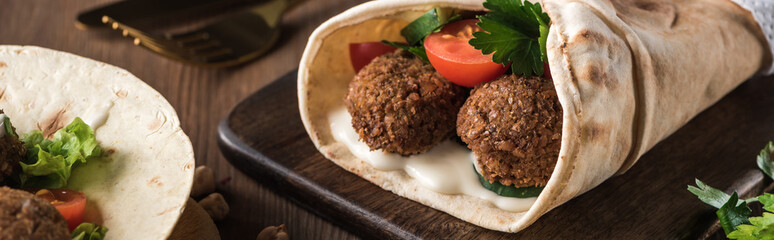 close up view of falafel with vegetables and sauce on pita on wooden table, panoramic shot