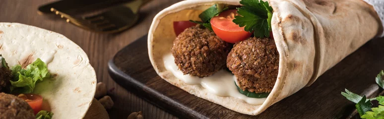 Fotobehang close up view of falafel with vegetables and sauce on pita on wooden table, panoramic shot © LIGHTFIELD STUDIOS