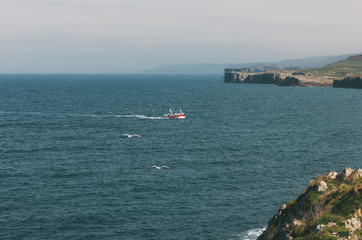 Fishing boat sailing in front of the cliffs of Llanes in Asturias