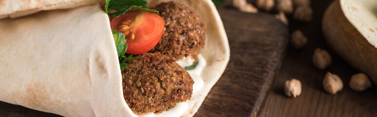 close up view of falafel with vegetables and sauce wrapped in pita on wooden table, panoramic shot