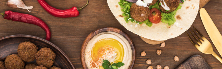 top view of falafel with vegetables and hummus on wooden table, panoramic shot