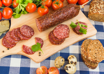 Sliced salami with bread, cherry tomatoes and quail eggs on table
