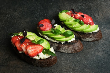 Toast or sandwich with avocado, cheese, strawberries, herbs and seeds on a dark background. An idea for bruschetta or for a healthy snack. Healthy vegan breakfast.