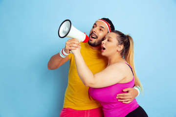Young pretty caucasian couple in bright clothes training on blue background Concept of sport, human emotions, expression, healthy lifestyle, relation, family. Sales. Calling together in mouthpeace.