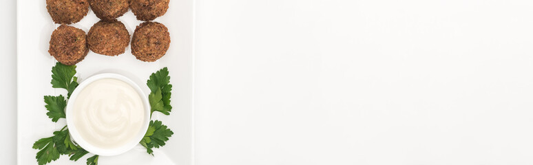 top view of falafel balls on plate with sauce and parsley on white background, panoramic shot