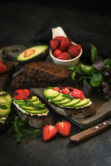 Toast or sandwich with avocado, cheese, strawberries, herbs and seeds on a dark background. An idea for bruschetta or for a healthy snack. Healthy vegan breakfast.