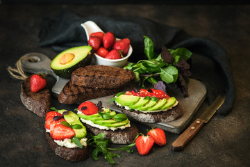 Toast or sandwich with avocado, cheese, strawberries, herbs and seeds on a dark background. An idea for bruschetta or for a healthy snack. Healthy vegan breakfast.