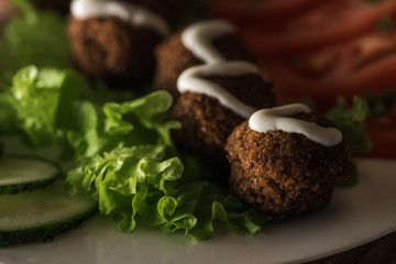 close up view of falafel with sauce on plate with sliced vegetables in dark, panoramic shot
