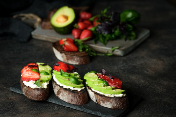 Toast or sandwich with avocado, cheese, strawberries, herbs and seeds on a dark background. An idea for bruschetta or for a healthy snack. Healthy vegan breakfast.