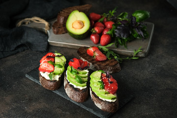 Toast or sandwich with avocado, cheese, strawberries, herbs and seeds on a dark background. An idea for bruschetta or for a healthy snack. Healthy vegan breakfast.
