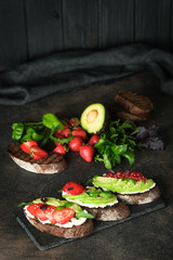 Toast or sandwich with avocado, cheese, strawberries, herbs and seeds on a dark background. An idea for bruschetta or for a healthy snack. Healthy vegan breakfast.