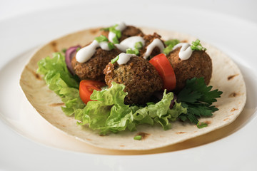 close up view of falafel with sauce on pita with vegetables in white plate