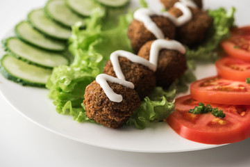 close up view of falafel with sauce on plate with sliced vegetables on white background