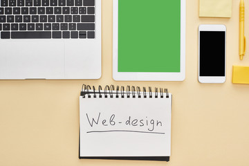 flat lay with gadgets and web design lettering in notepad on yellow background