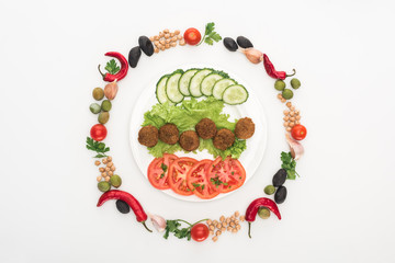 top view of vegetables arranged in round frame around falafel on plate on white background