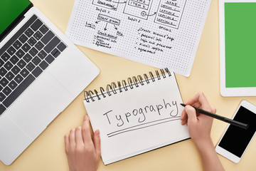 Obraz premium cropped view of designer writing typography lettering in notebook near website design template and gadgets on yellow background