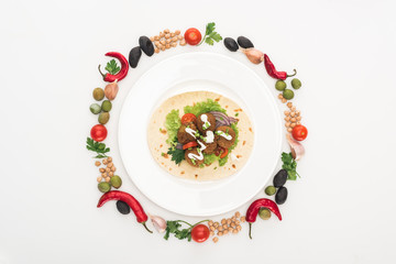 top view of vegetables arranged in round frame around falafel on pita on plate on white background