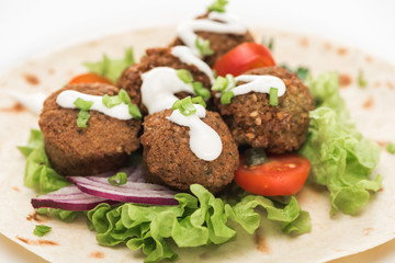 close up view of fresh falafel balls on pita with vegetables and sauce on white background
