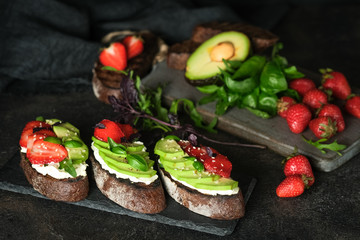 Toast or sandwich with avocado, cheese, strawberries, herbs and seeds on a dark background. An idea for bruschetta or for a healthy snack. Healthy vegan breakfast.