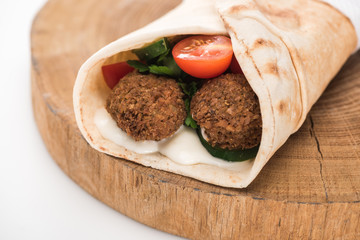 close up view of fresh falafel balls in pita with vegetables and sauce on wooden board on white background