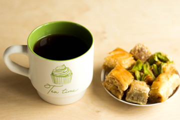 Cakes and tea in a mug. On the wooden table top are a mug of tea and a plate of Oriental sweets