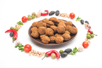 chickpea, garlic, cherry tomatoes, parsley, olives, chili pepper, green onion arranged in round frame around falafel balls on plate on white background