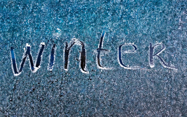 word winter scraped on frosty glass covered with white crystals and placed on the window on a winter cold clear morning