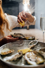 Oysters in a round metal plate with ice, lemon. Female’s hand pours open lemon on oysters....