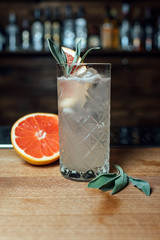 Cocktail with a grapefruit on a bar counter in a night club. Fresh cocktail on a bar with bottles on the background