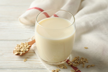 Glass of oat milk, spoon with oatmeal seeds and napkin on white, wooden background, space for text. Closeup