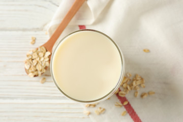 Glass of oat milk, spoon with oatmeal seeds and napkin on white, wooden background, top view. Closeup