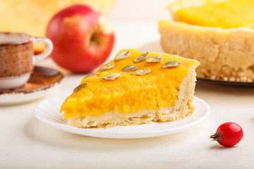 Traditional american sweet pumpkin pie decorated with hawthorn red berries and pumpkin seeds with cup of coffee on a white wooden background. side view, selective focus.