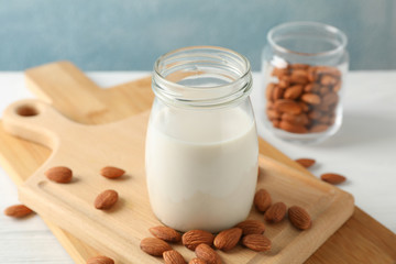 Glass of almond milk, almond seeds on white table again blue background, space for text. Closeup