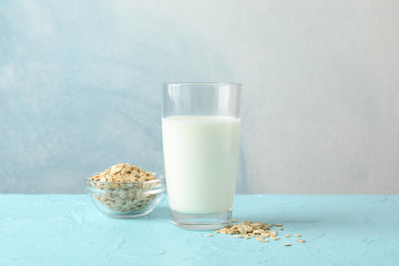 Glass of oat milk and oatmeal seeds on blue background, space for text