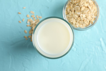 Glass of oat milk and oatmeal seeds on blue background, space for text. Top view