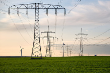 Stromtrasse, Hochspannungsmasten hintereinander aufgereiht bis zum Horizont auf einer grünen...